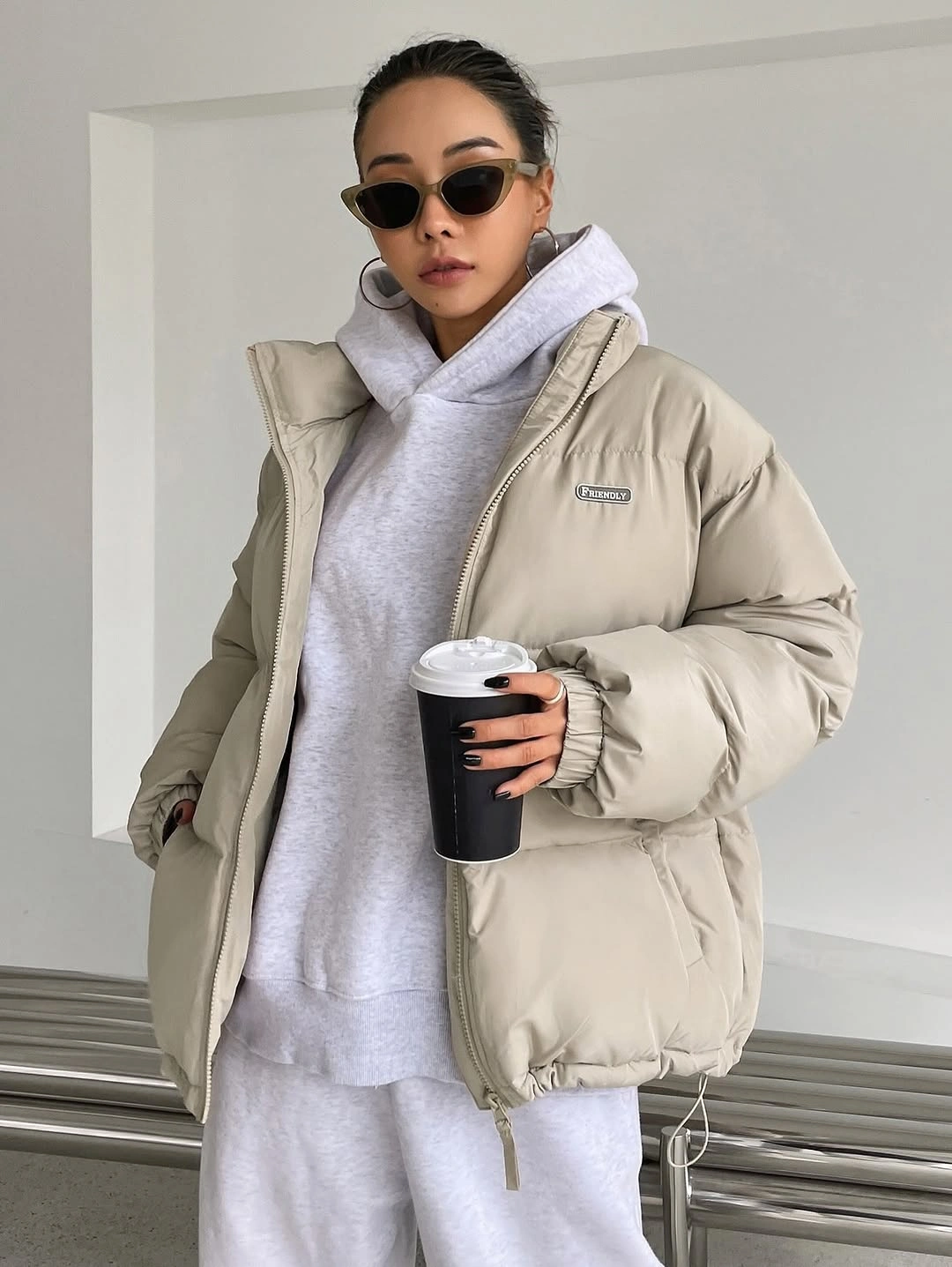 Pale puffer jacket over gray hoodie and sweatpants with angular sunglasses
