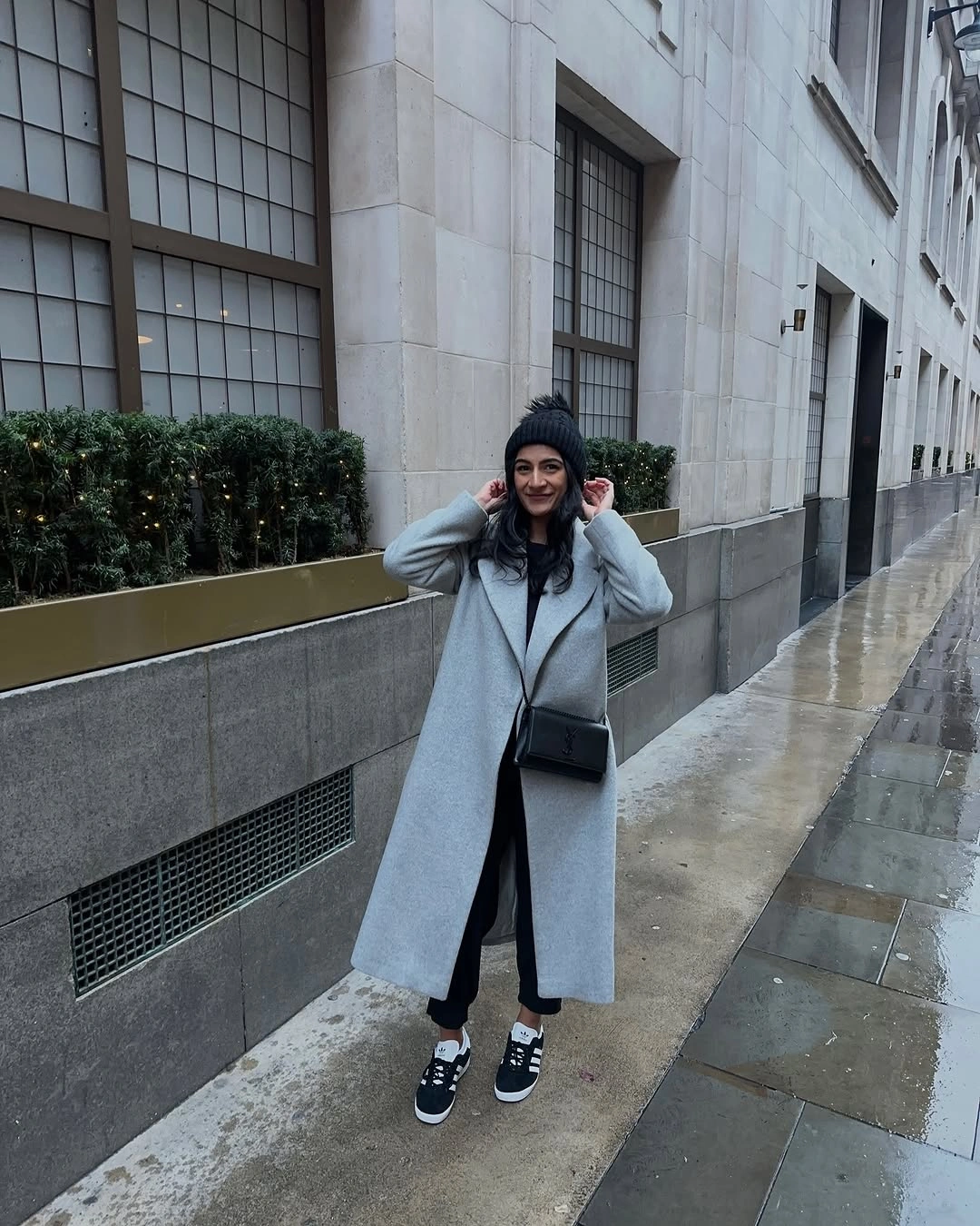 Long light gray coat with dark beanie, black crossbody bag, and sneakers
