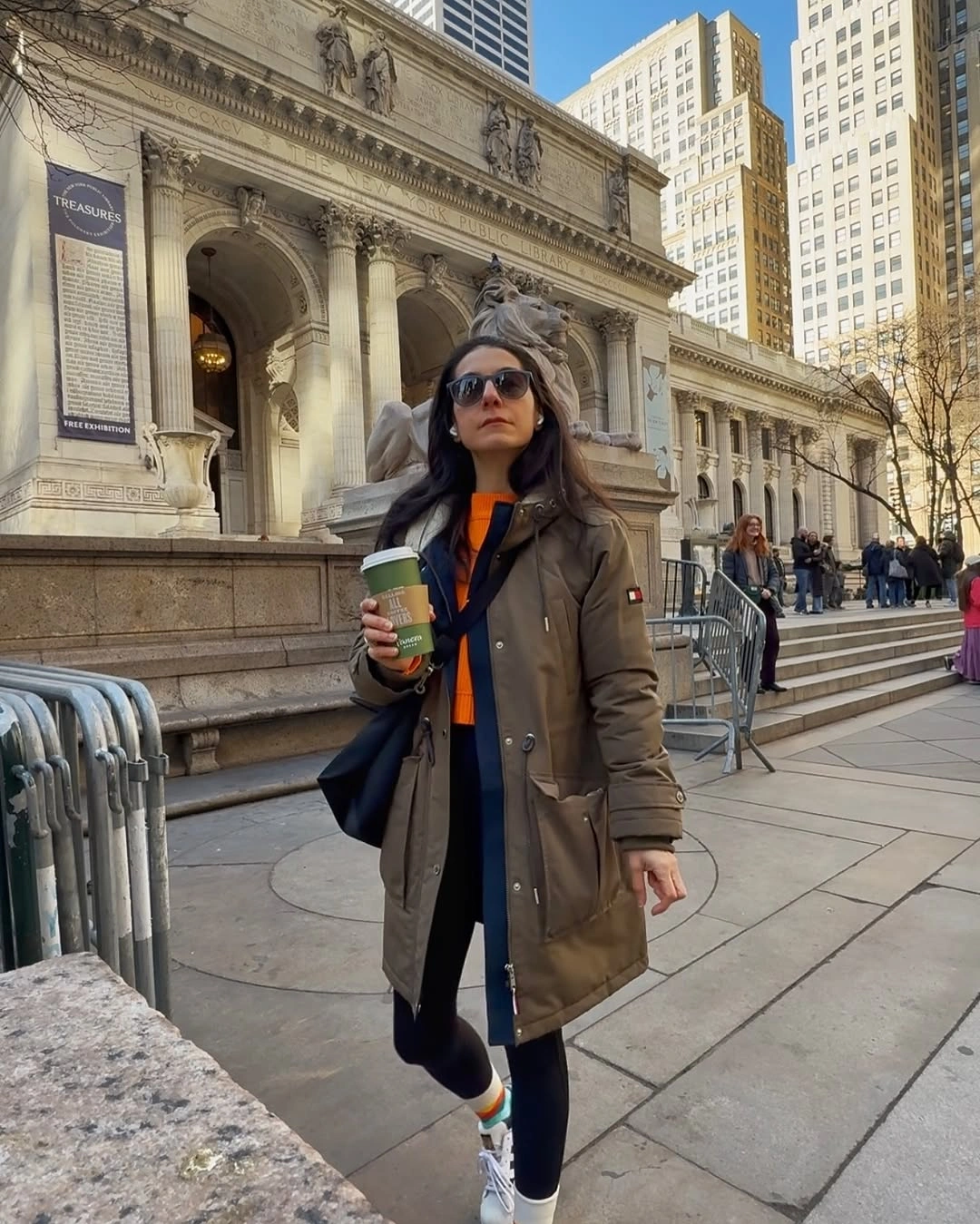 Olive parka with orange and navy layers, gray head covering, and white sneakers