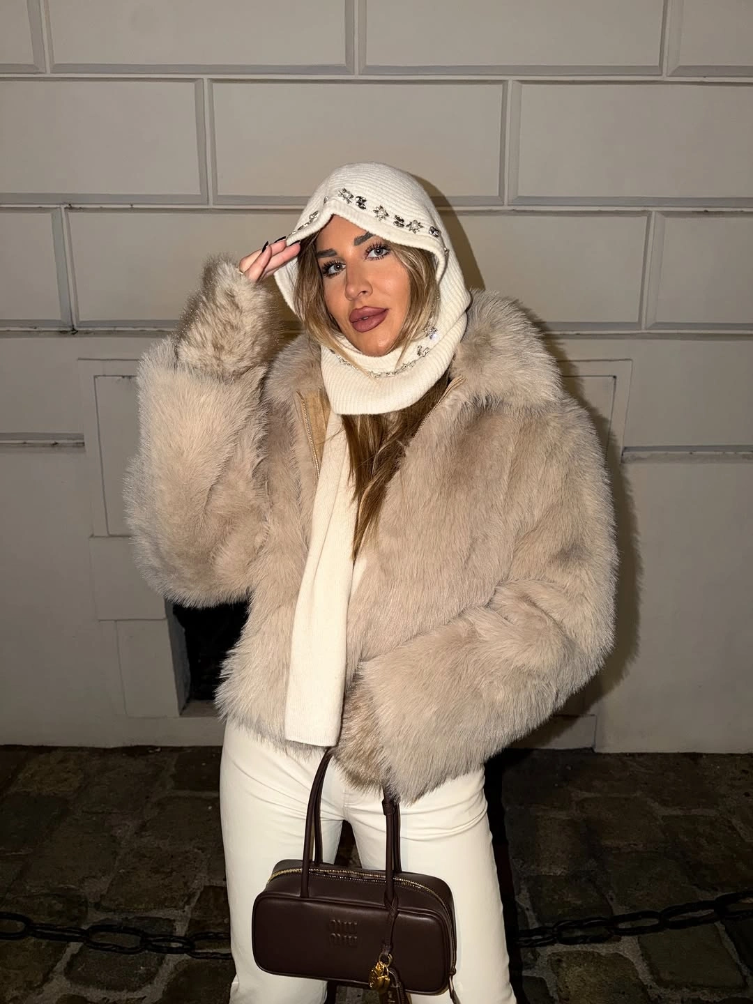 Pale plush jacket with cream knit head covering and dark brown handbag