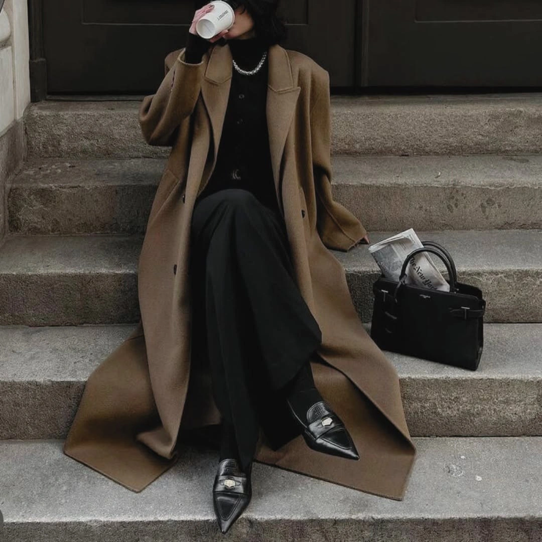 Long camel coat over black layers with pointed shoes and structured handbag
