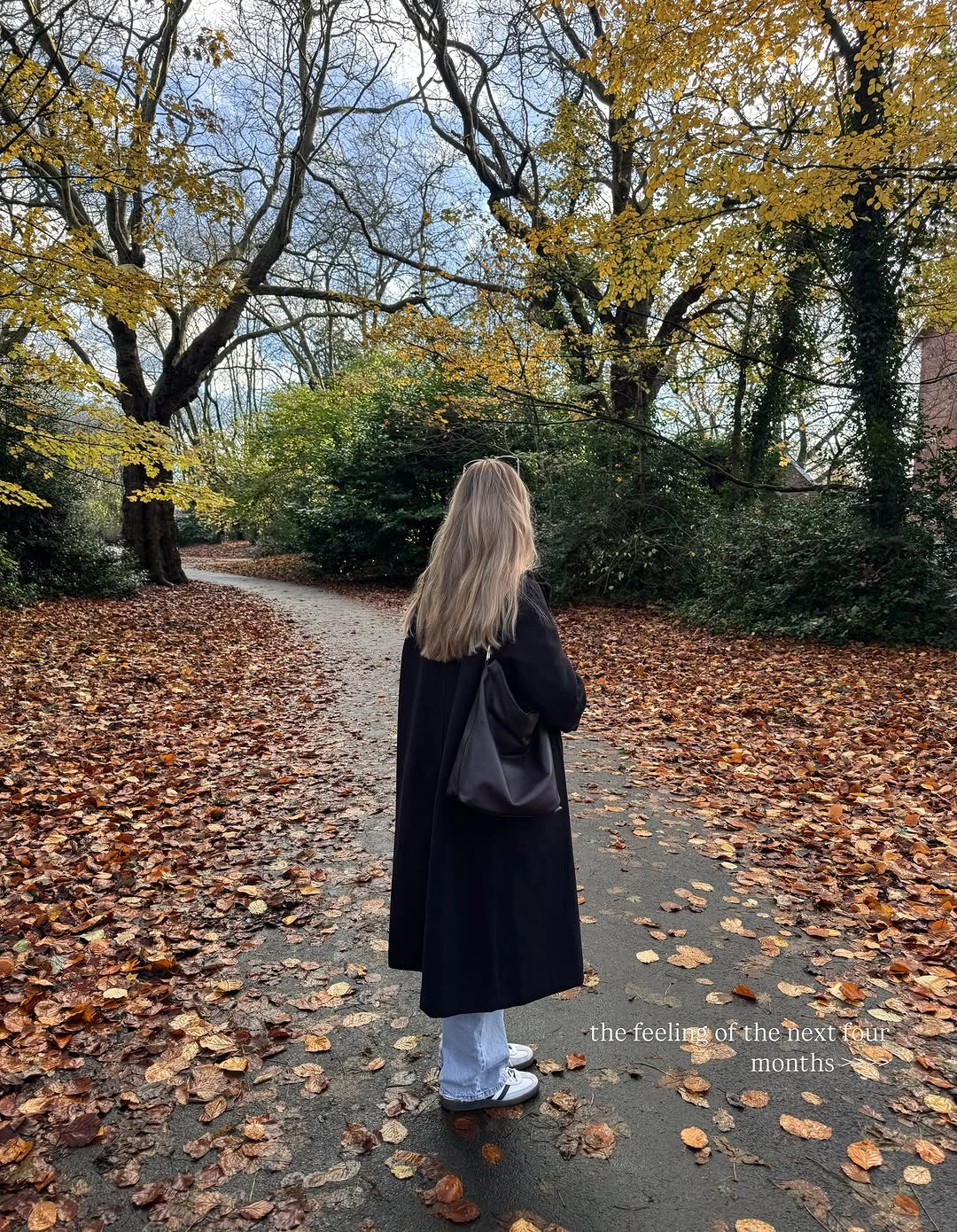 Back view of long dark coat, light blue jeans, and shoulder bag