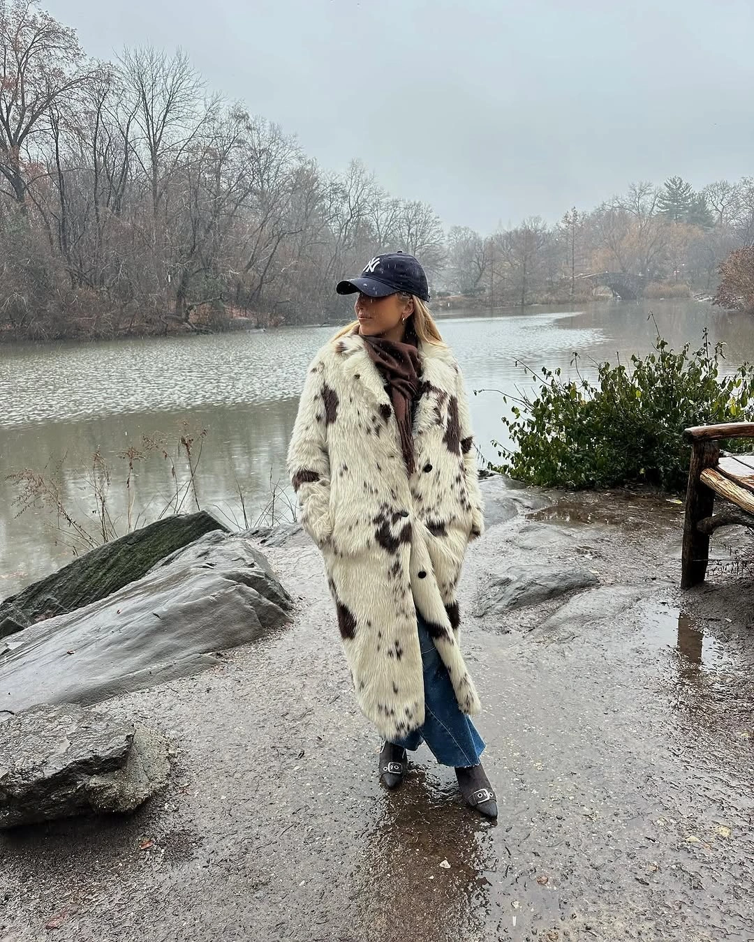 Long cream spotted coat with dark cap, brown scarf, and blue jeans