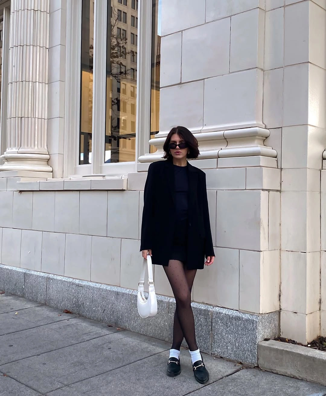 Oversized black blazer with dotted tights, white socks, loafers, and white handbag