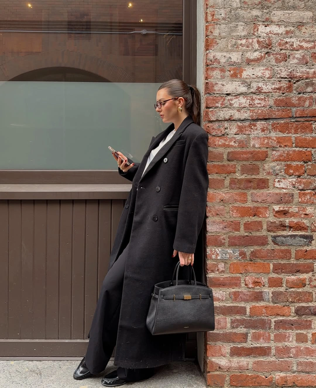 Long black double-breasted coat with black handbag and dark trousers
