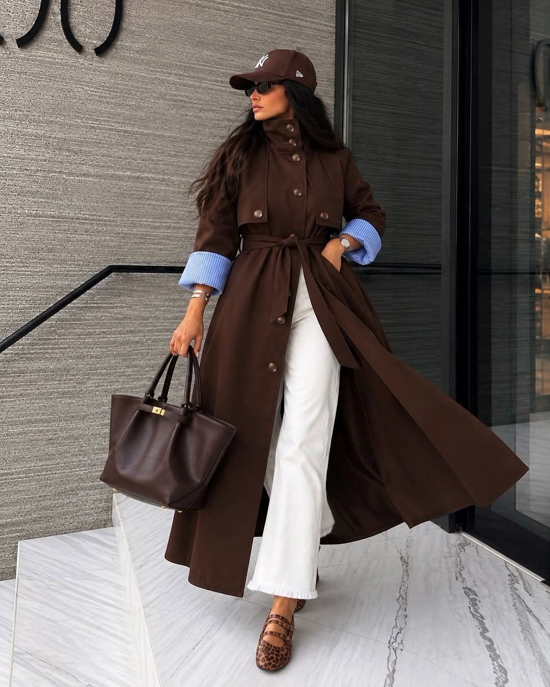 Belted brown coat, white wide-leg trousers, baseball cap, and brown tote