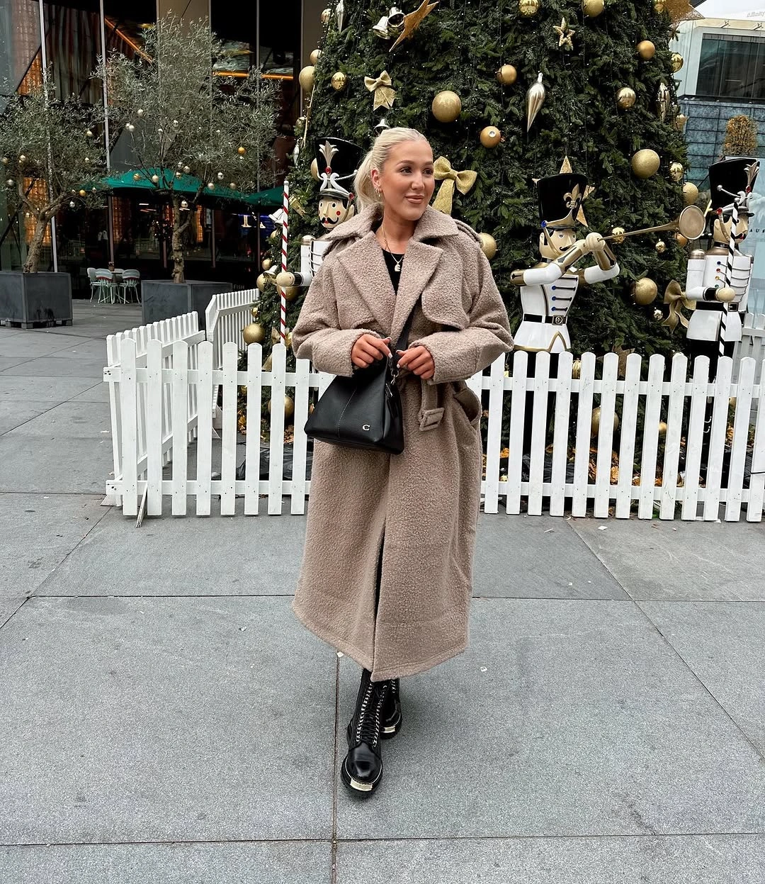 Long taupe textured coat with black lace-up boots and black handbag