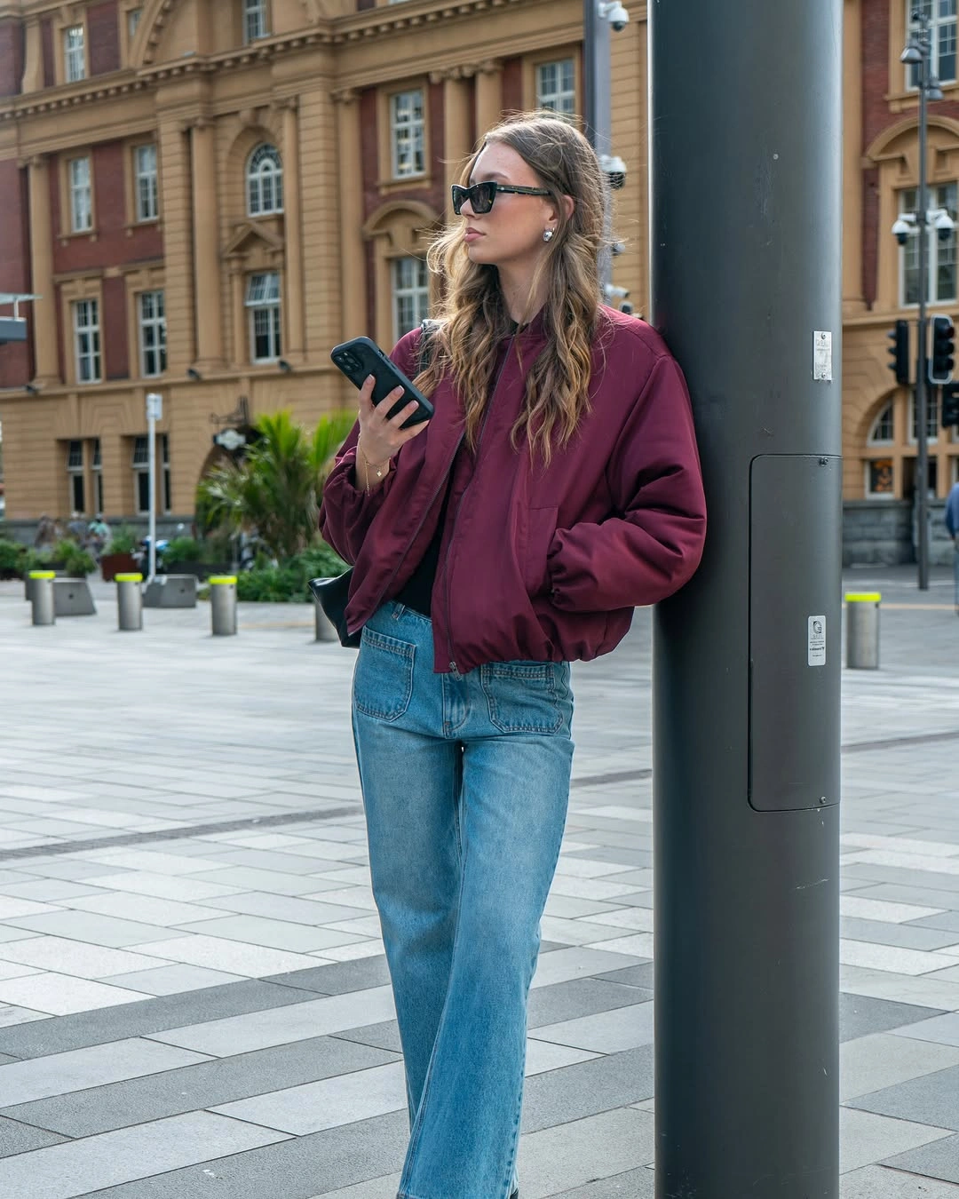 Burgundy bomber jacket with light blue relaxed jeans and dark sunglasses