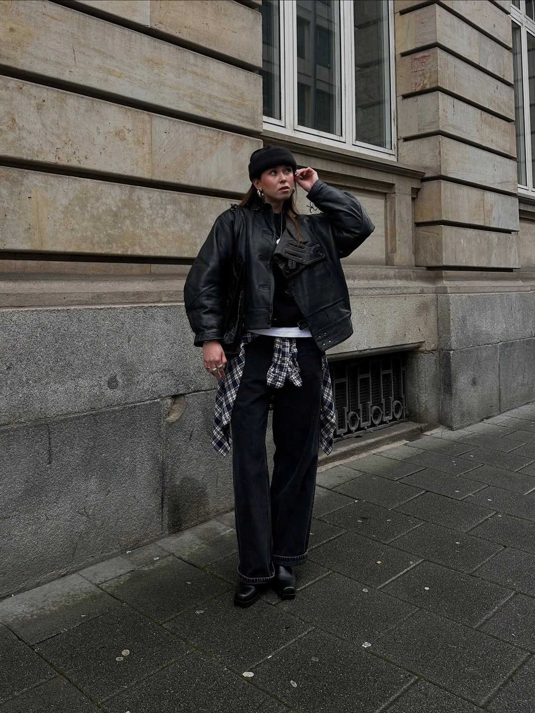 Oversized black leather look jacket with beanie wide trousers and tied plaid shirt