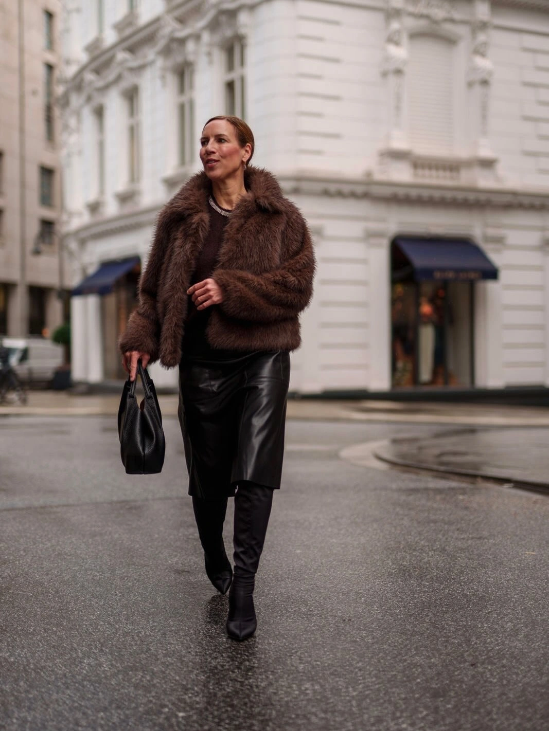 Brown plush jacket with black skirt dark tights tall boots and handbag