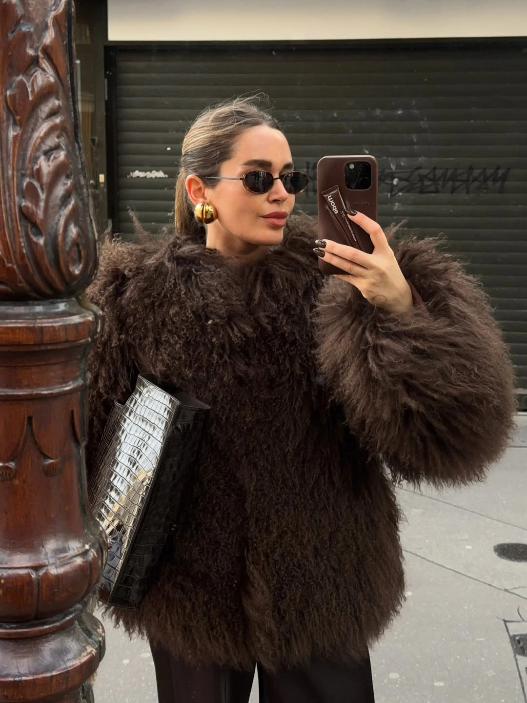 Dark brown shaggy coat with silver textured bag narrow sunglasses and gold earrings