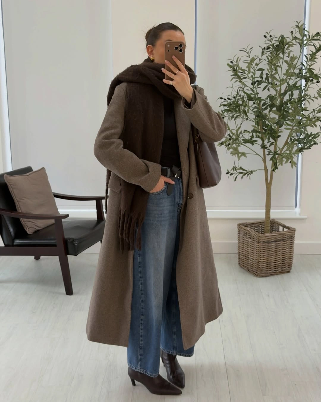 Long taupe brown coat with dark scarf blue jeans and pointed boots