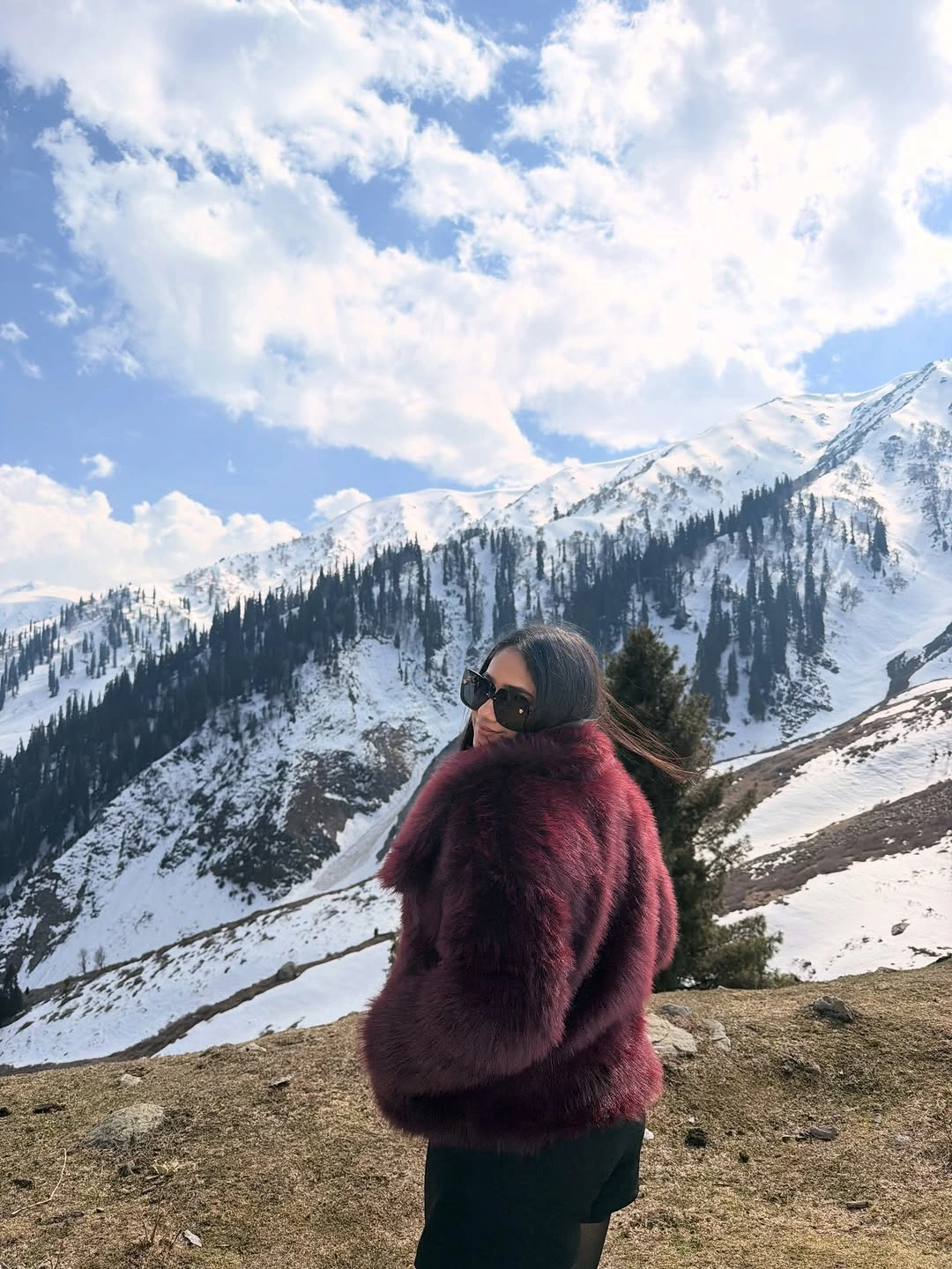Deep burgundy plush looking jacket with black sunglasses against snowy mountain landscape