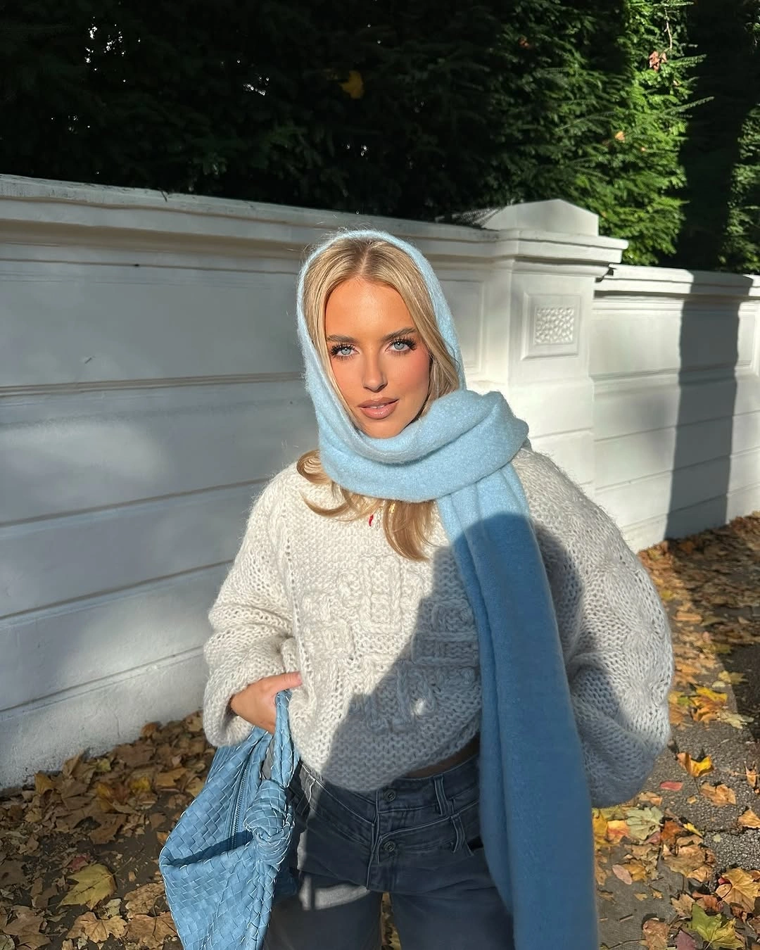 Cream cable-knit sweater with pale blue scarf, textured blue handbag, and jeans.