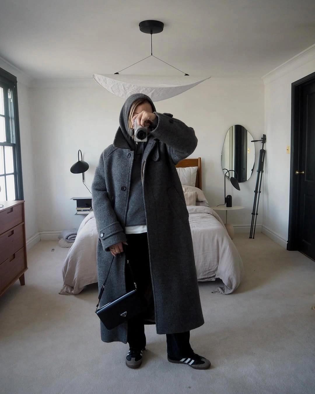 Long charcoal coat over dark hoodie, black trousers, and striped sneakers.