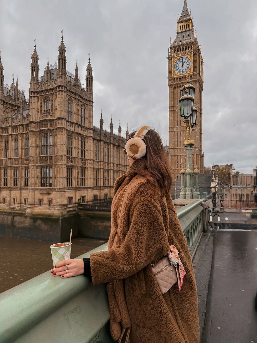 Oversized brown textured coat with cream earmuffs and pale quilted shoulder bag.