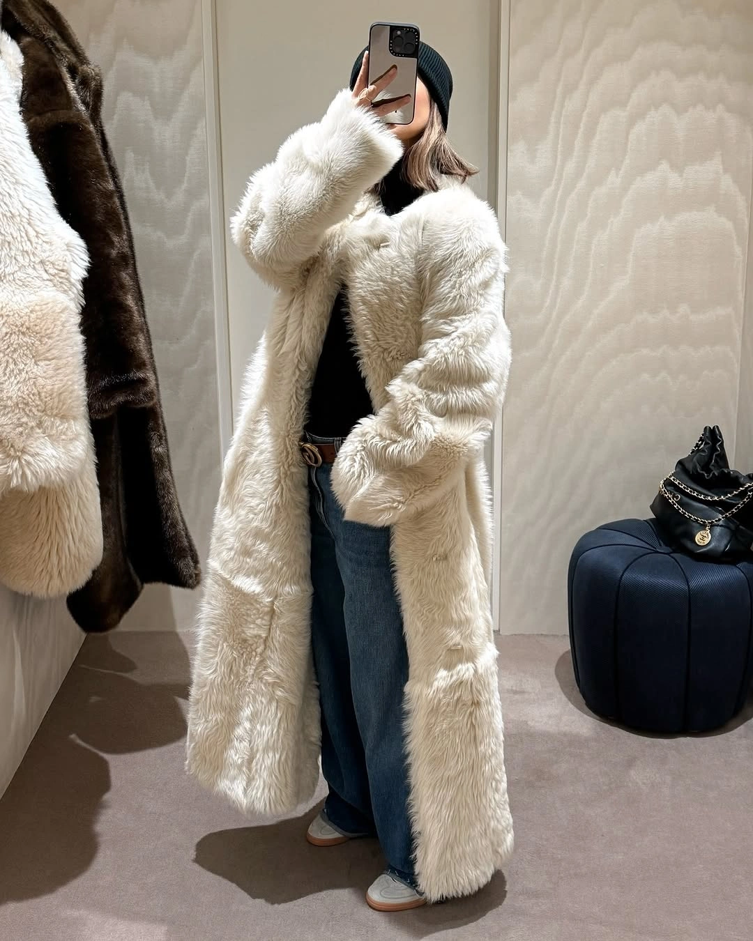 Long ivory fuzzy coat over black top, blue jeans, and dark beanie.