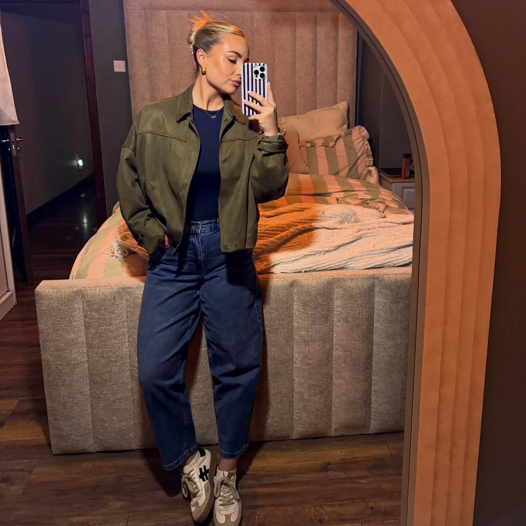 Olive cropped jacket over navy top, dark wide jeans, and light sneakers.