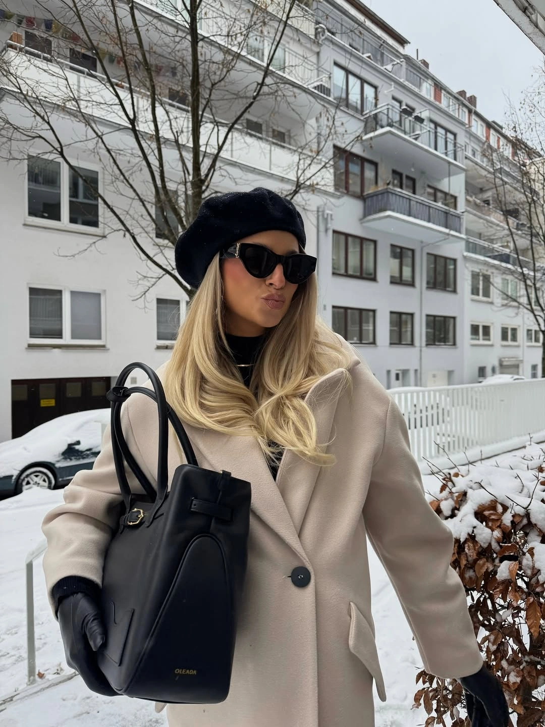 Cream coat with black beret, sunglasses, gloves, and large structured tote.