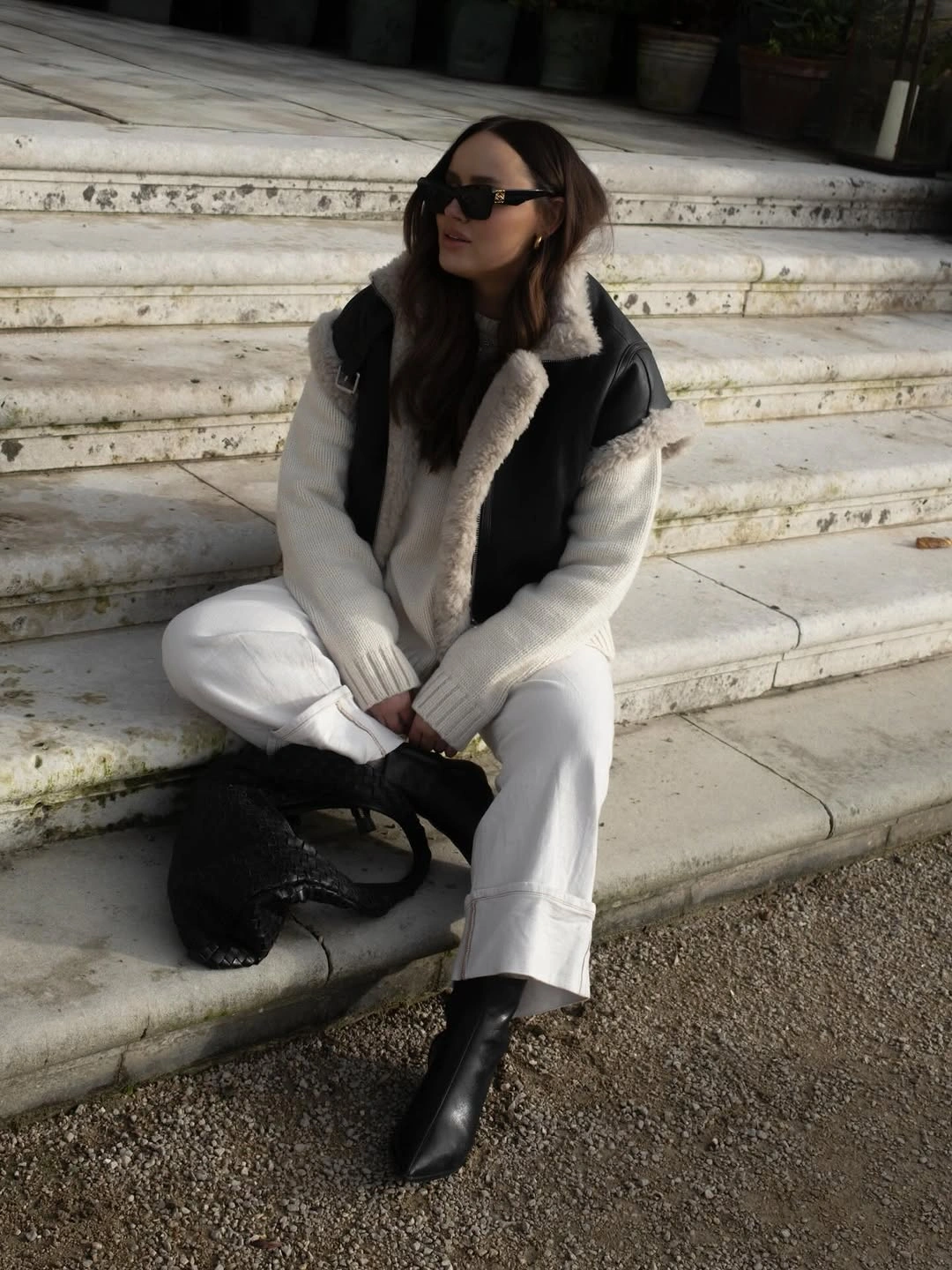 Dark fuzzy-trimmed vest over white sweater, cuffed trousers, and pointed black boots.