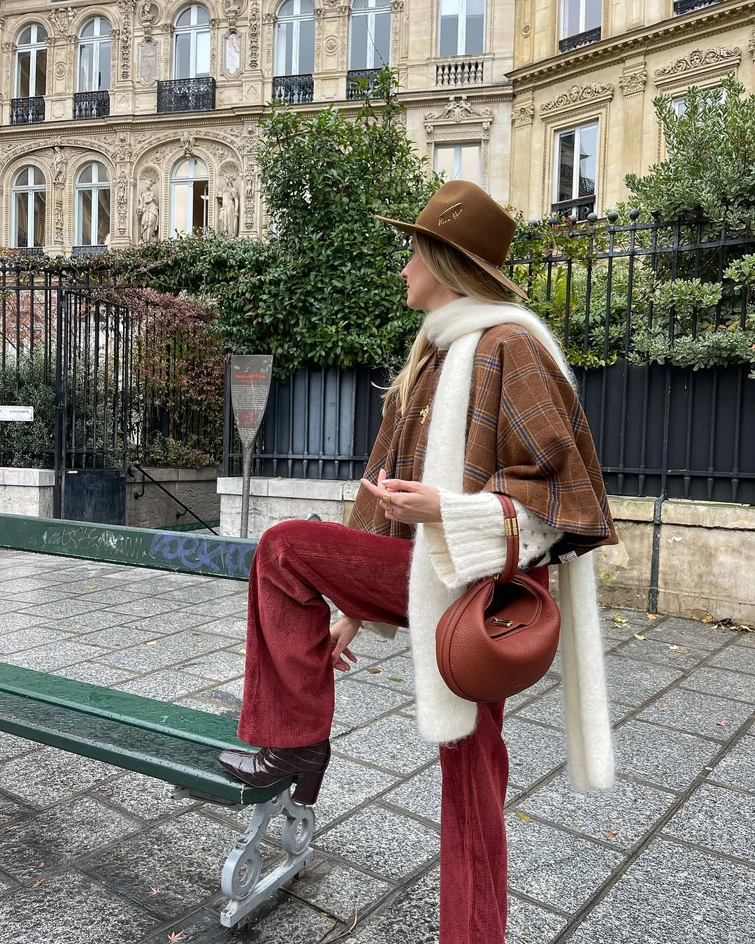 Brown plaid jacket, cream scarf, burgundy pants, brown hat, and rounded bag.
