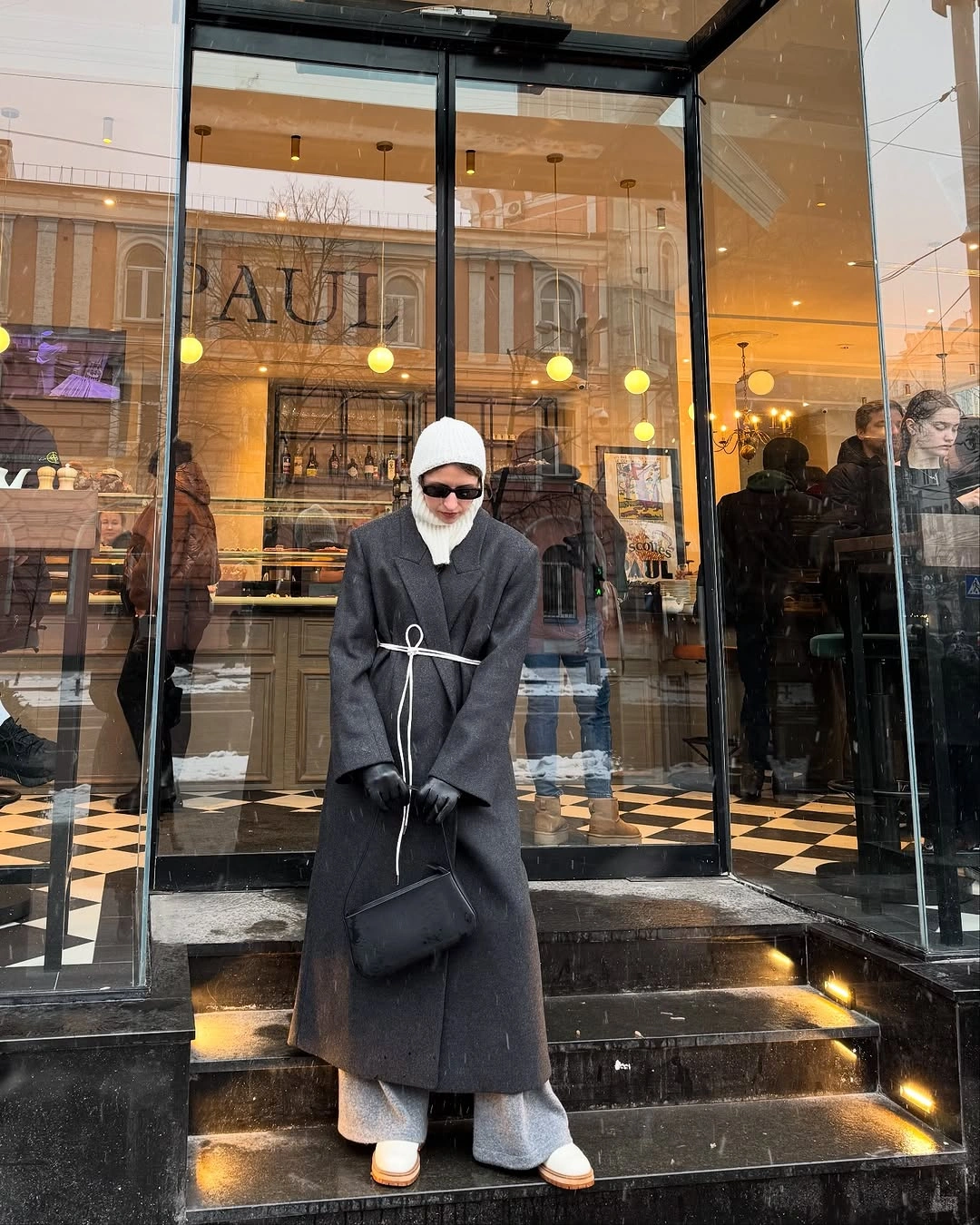 Charcoal long coat, gray trousers, white knit cap, gloves, and black handbag.