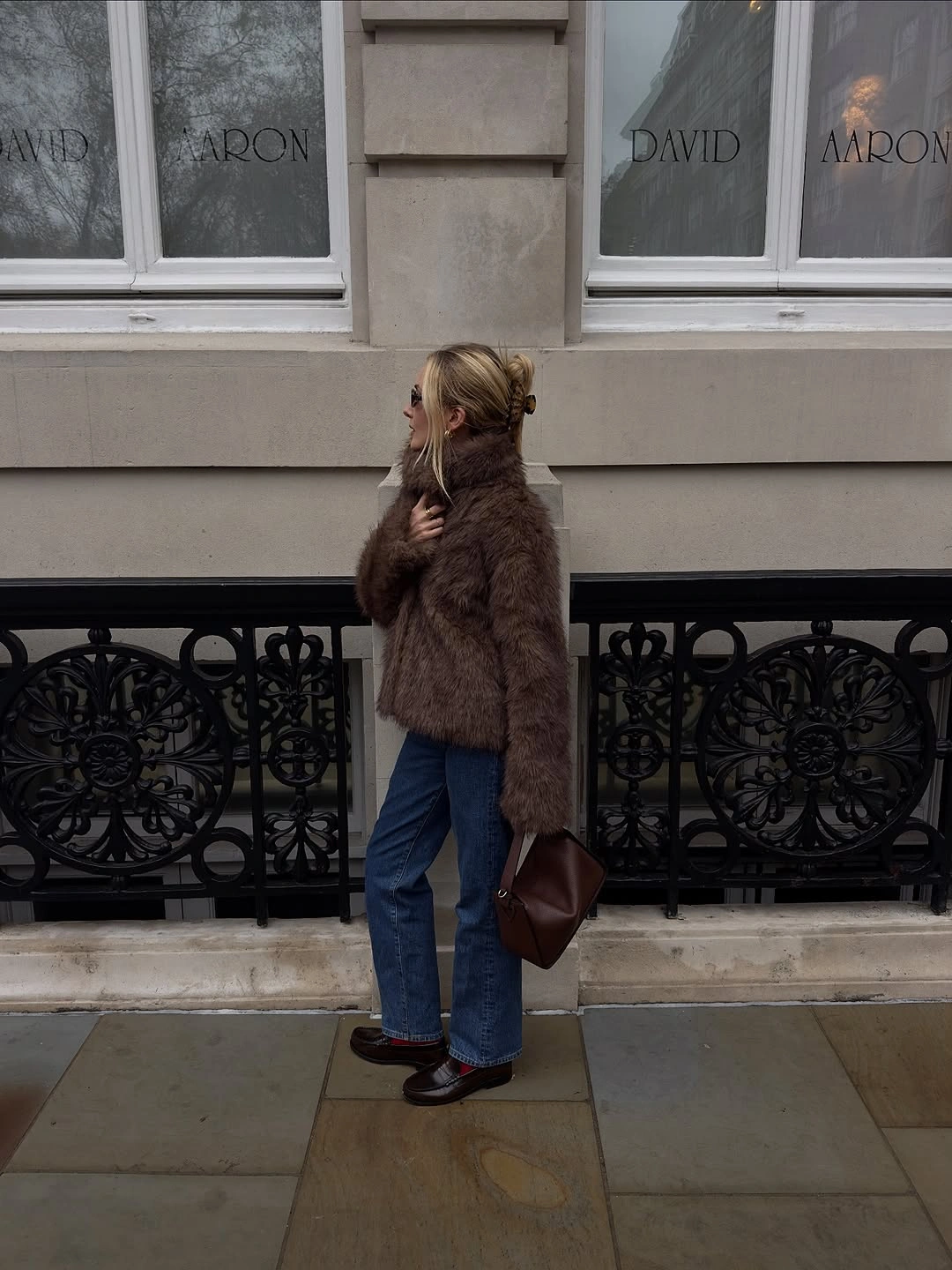 Fuzzy brown jacket with blue cuffed jeans, dark shoes, and brown handbag.