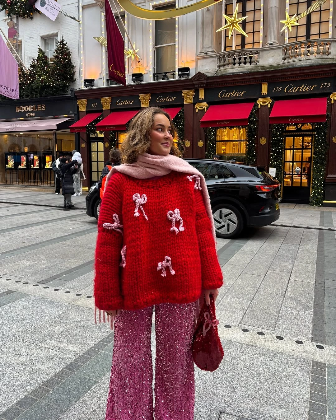 Red bow-decorated sweater, sparkling pink trousers, pink scarf, and red handbag.