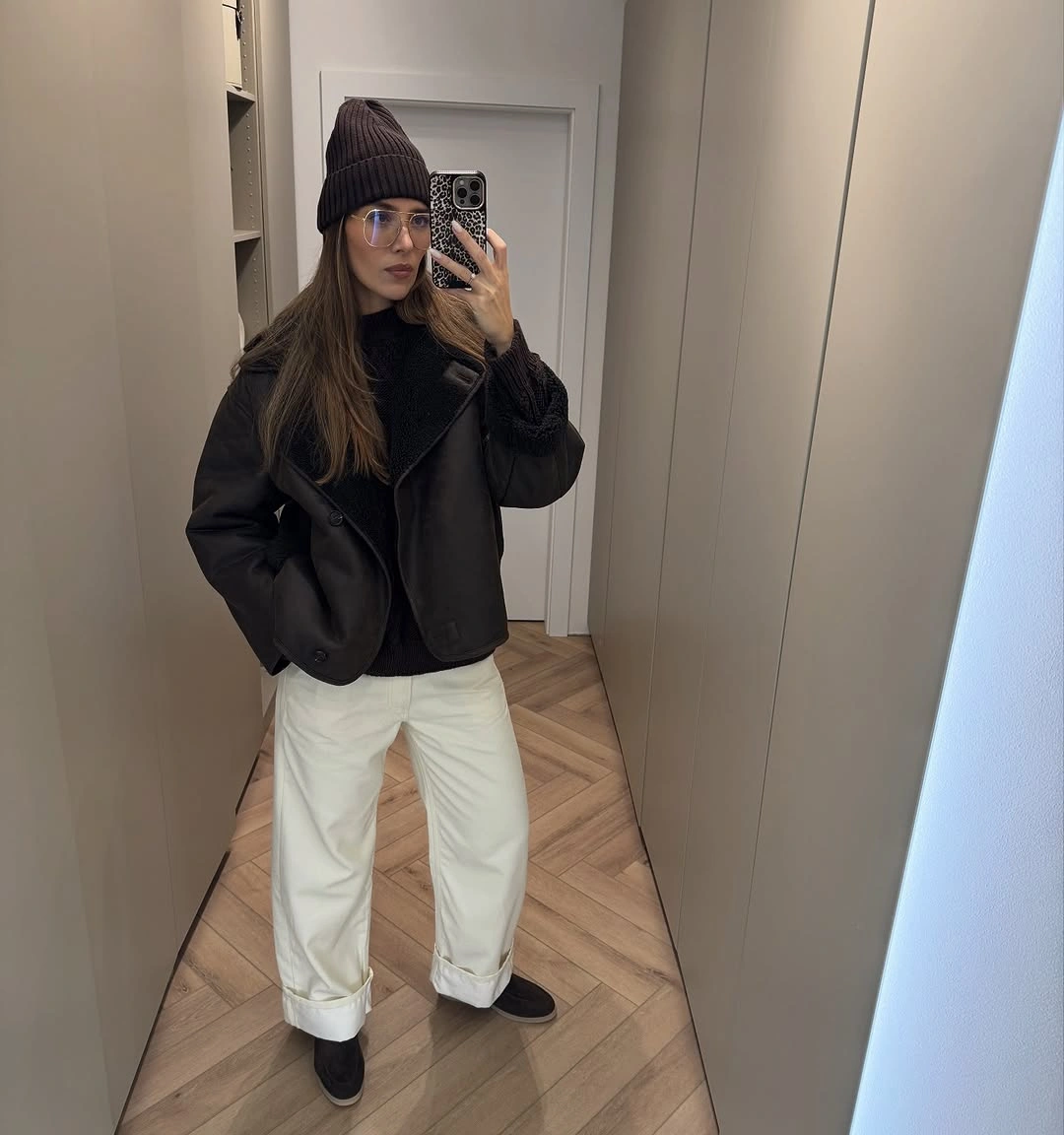 Short black jacket dark beanie ivory cuffed trousers and black shoes