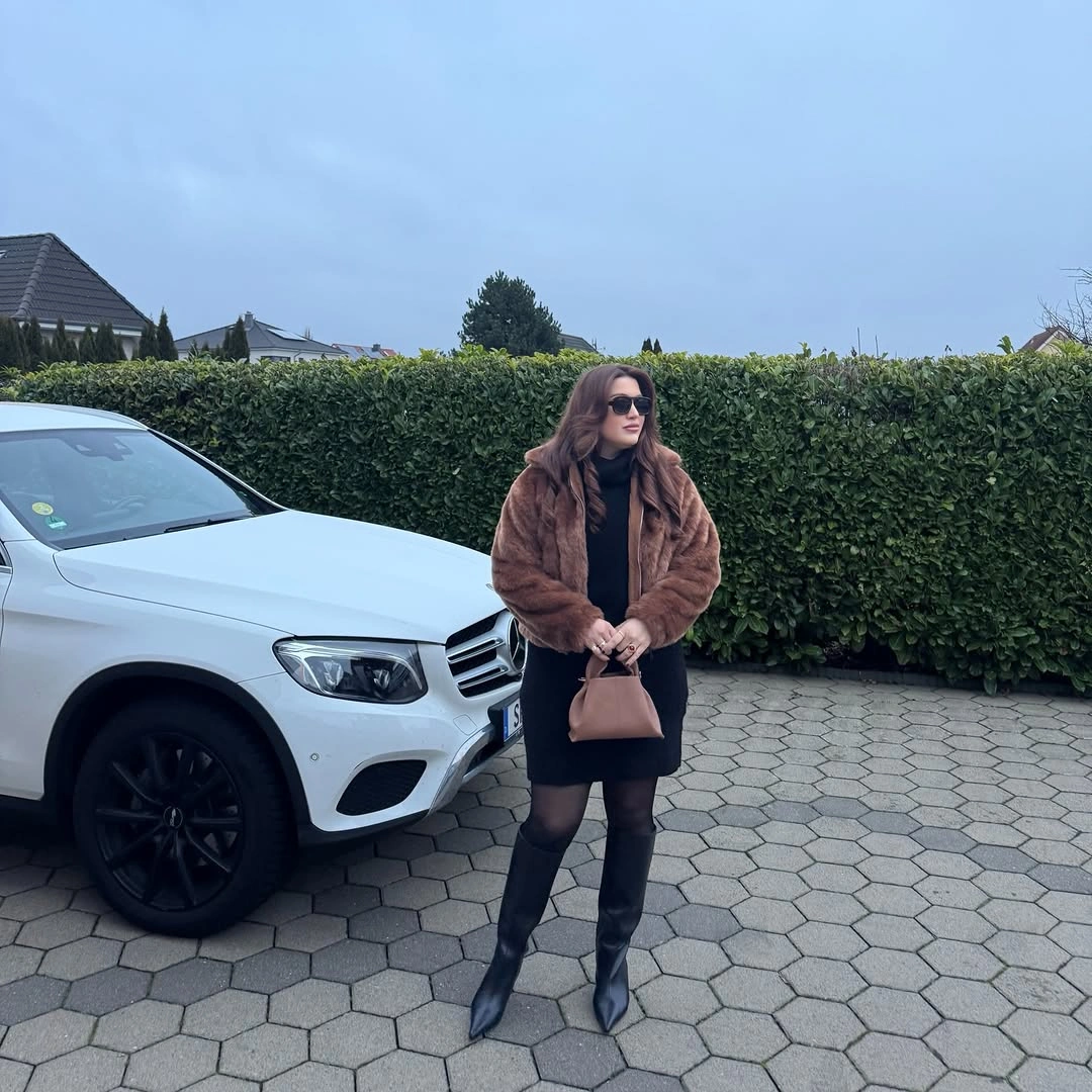 Short brown plush jacket black outfit sheer tights tall boots and handbag
