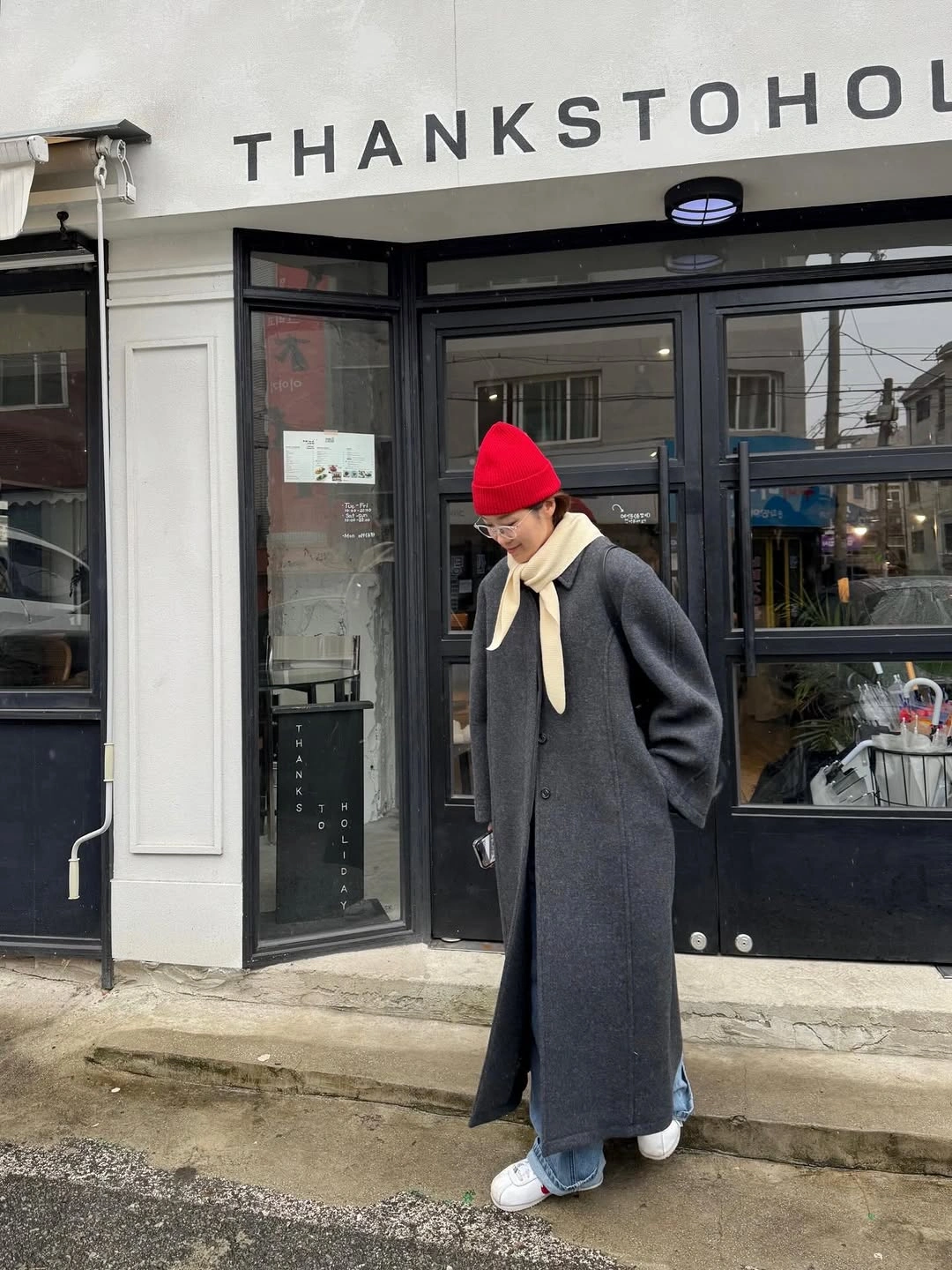 Long charcoal coat red knit beanie pale scarf blue jeans and sneakers
