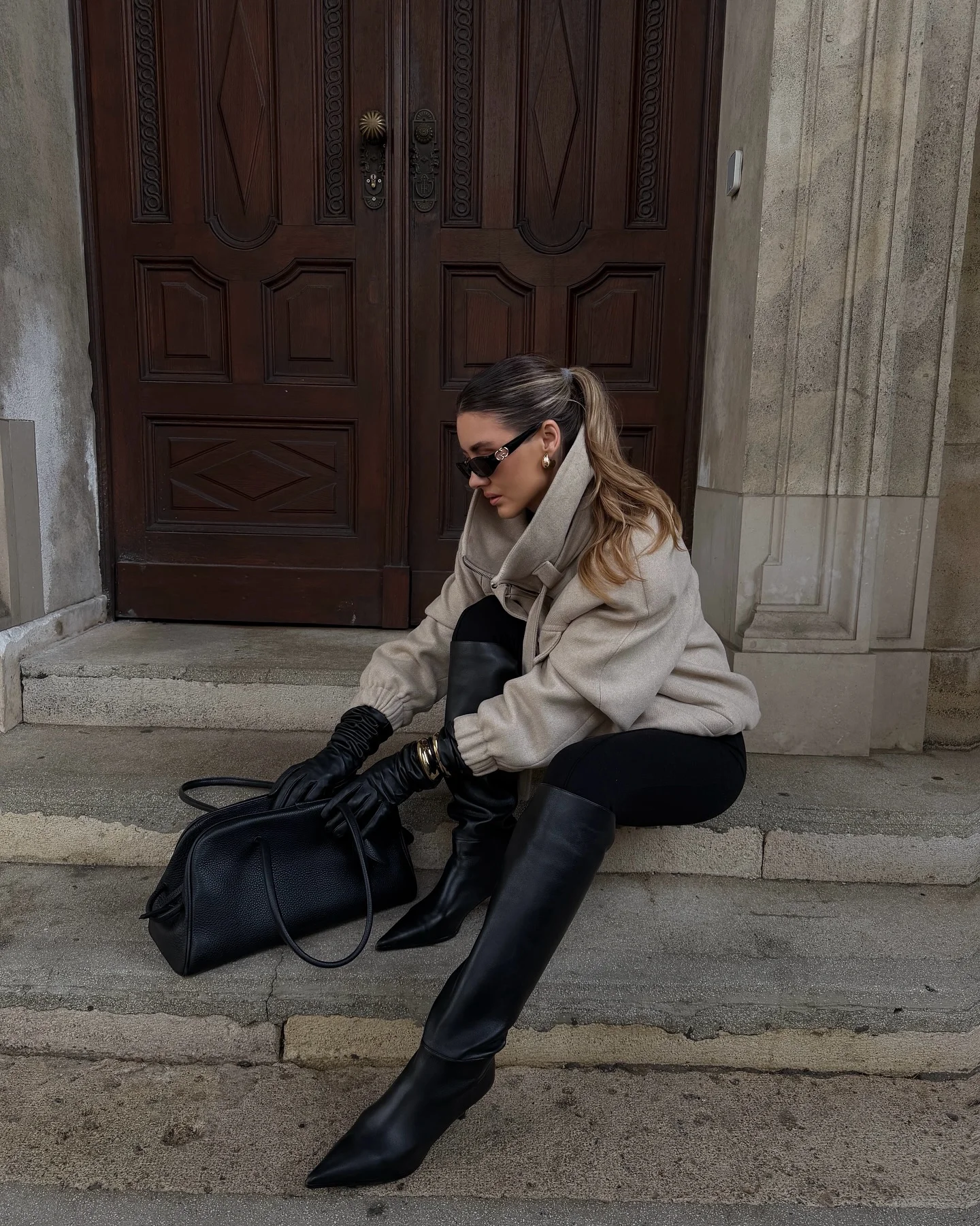 Oversized taupe jacket black gloves tall boots sunglasses and handbag
