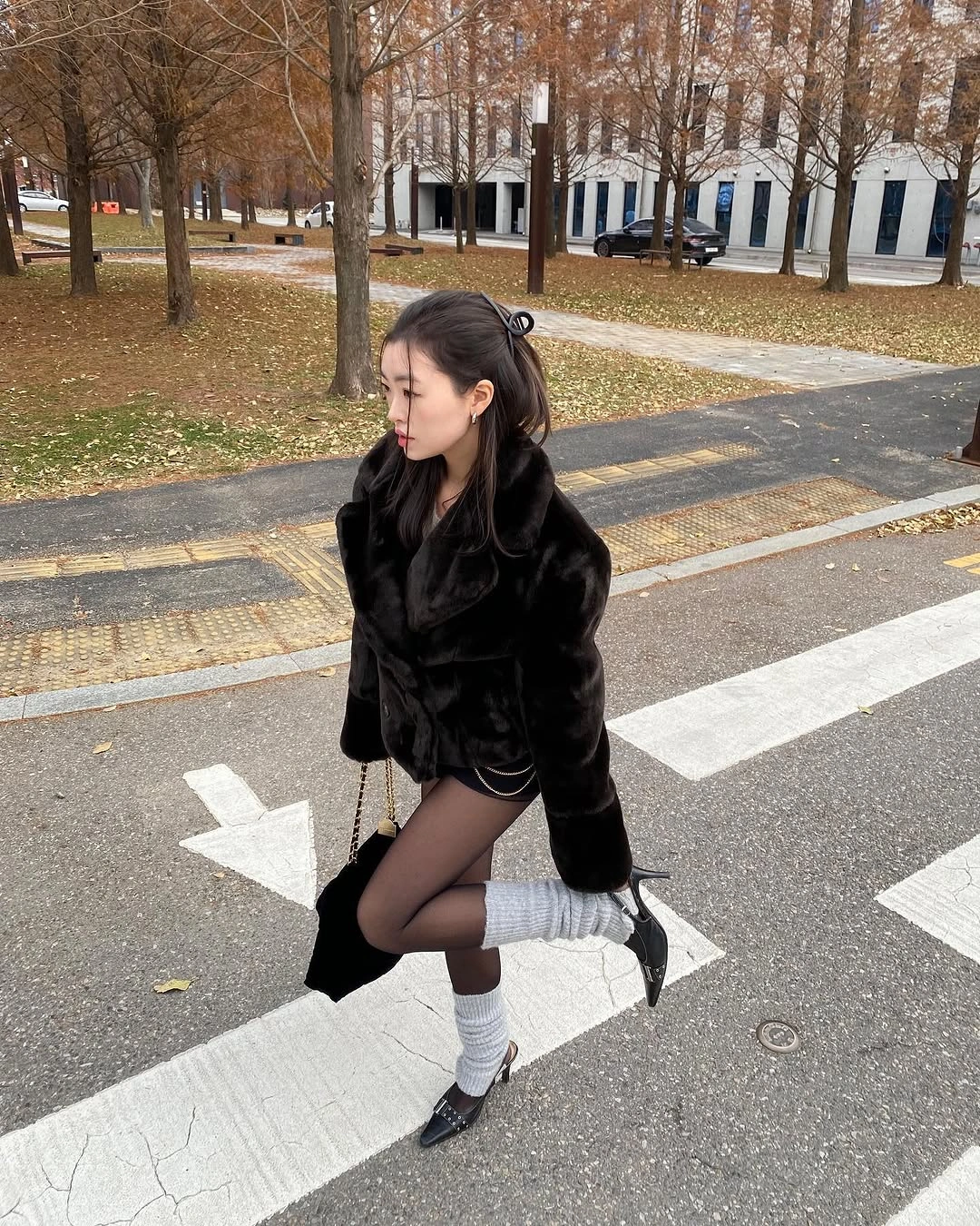 Short black plush jacket, dark tights, gray leg warmers and strap shoes