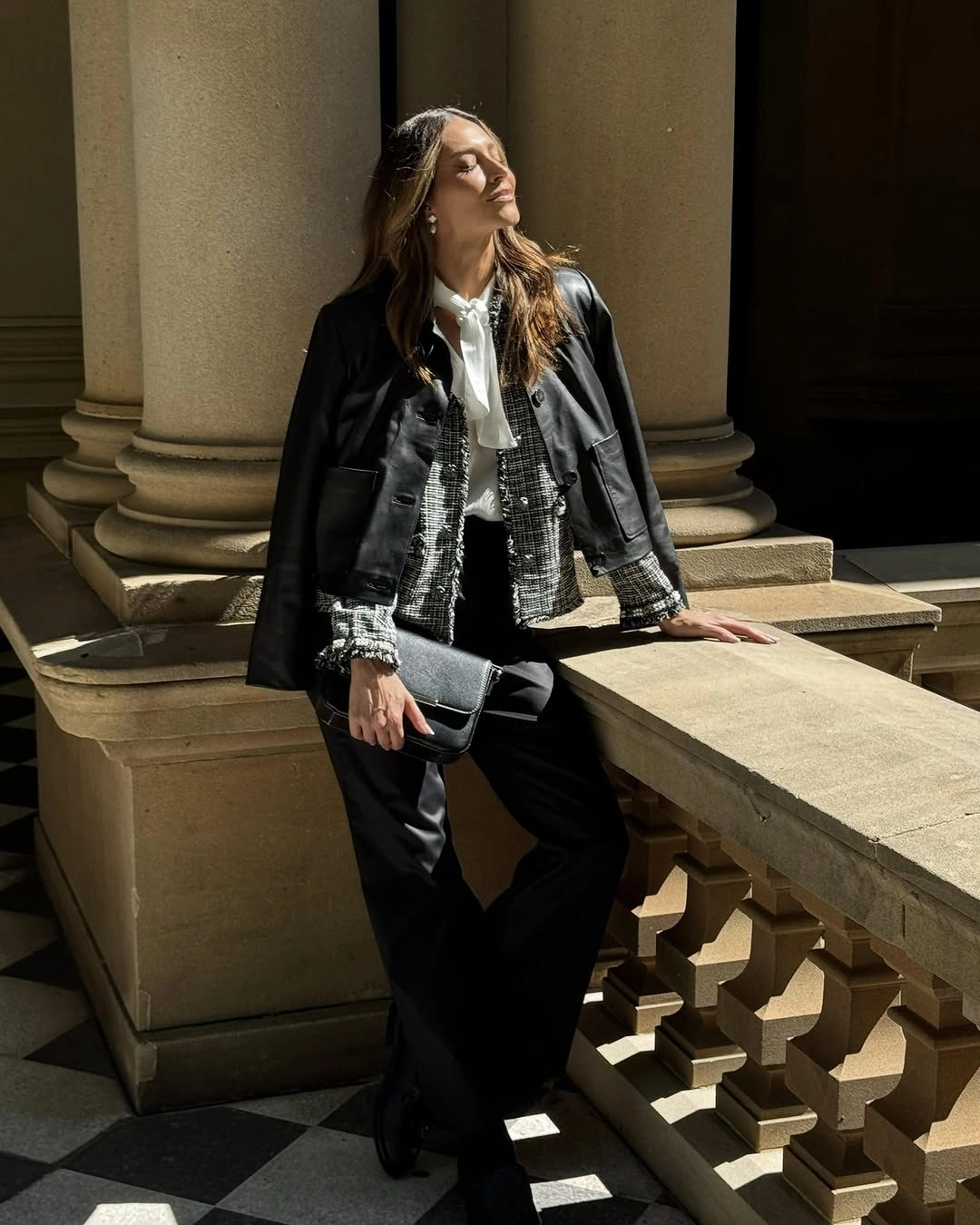 Black outer layer over patterned jacket, white blouse and wide trousers