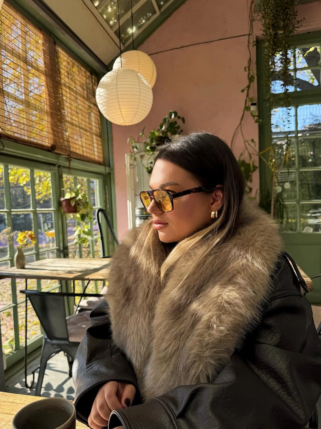 Black leather-look jacket with broad fuzzy collar and amber sunglasses