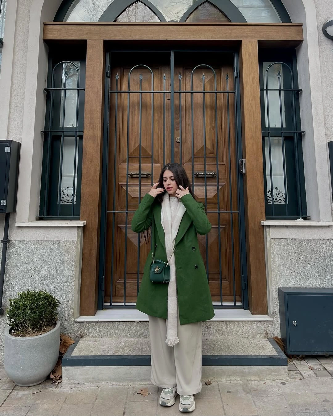 Green coat with cream scarf, wide trousers, sneakers, and matching bag