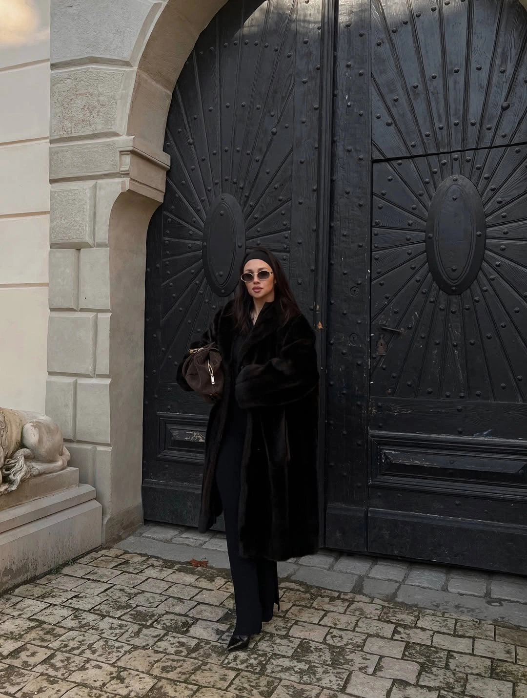 Long shaggy black coat with trousers, pointed shoes, and brown bag