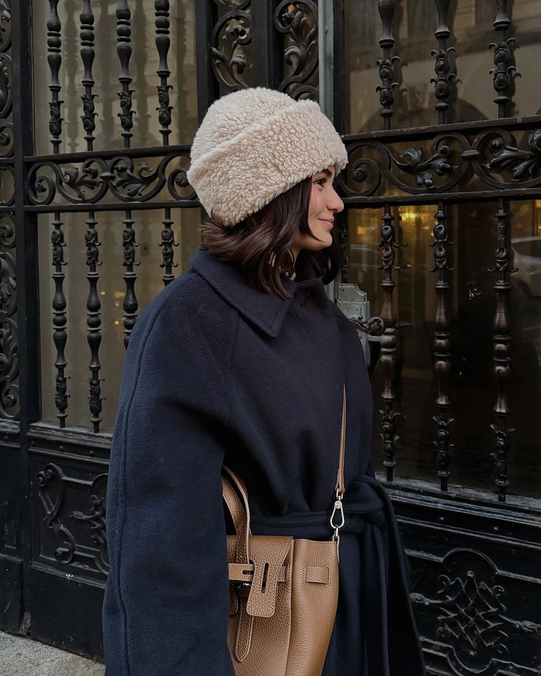 Navy belted coat, cream textured hat, and tan crossbody bag