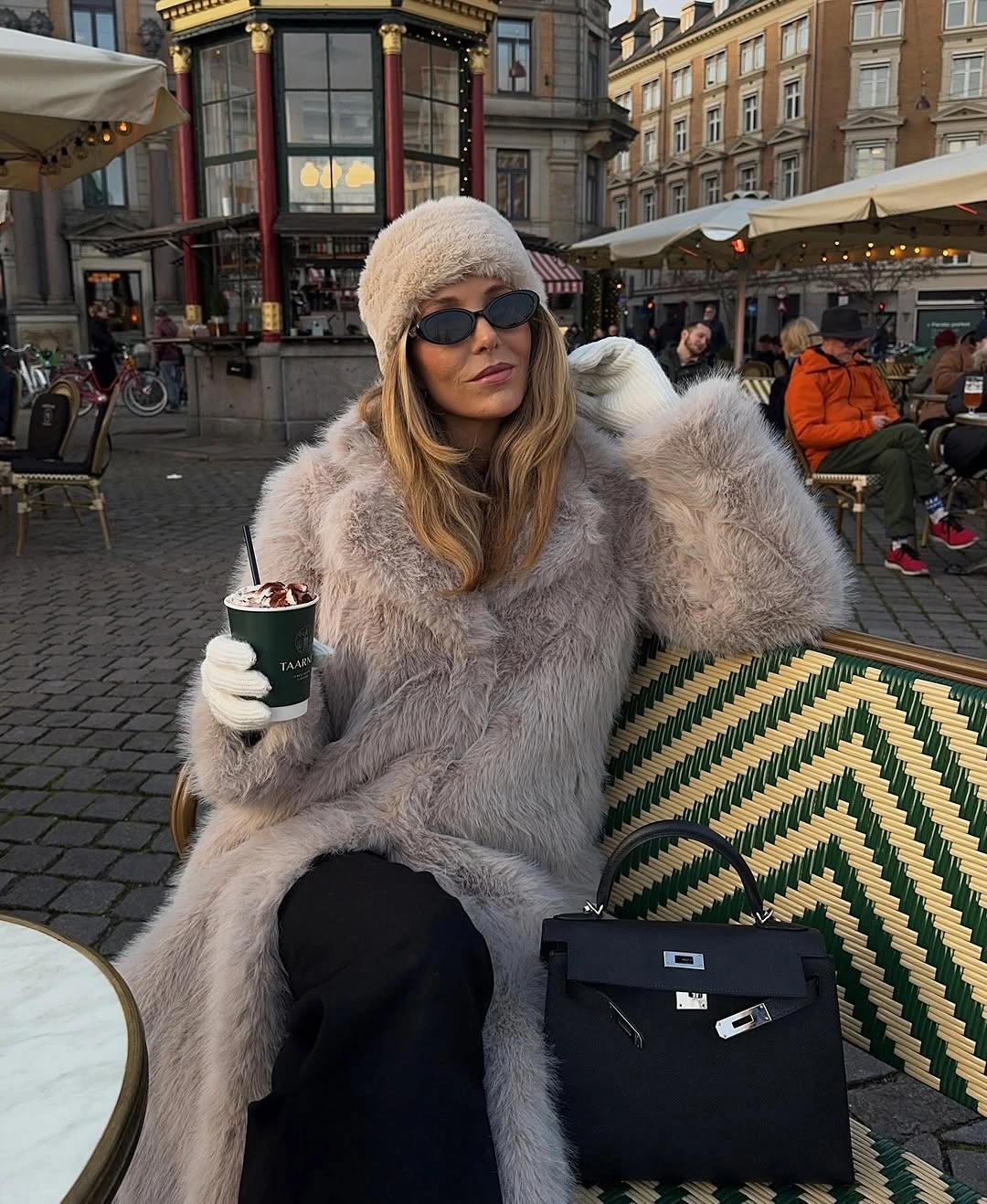Long shaggy gray coat, cream hat, black bag, and sunglasses