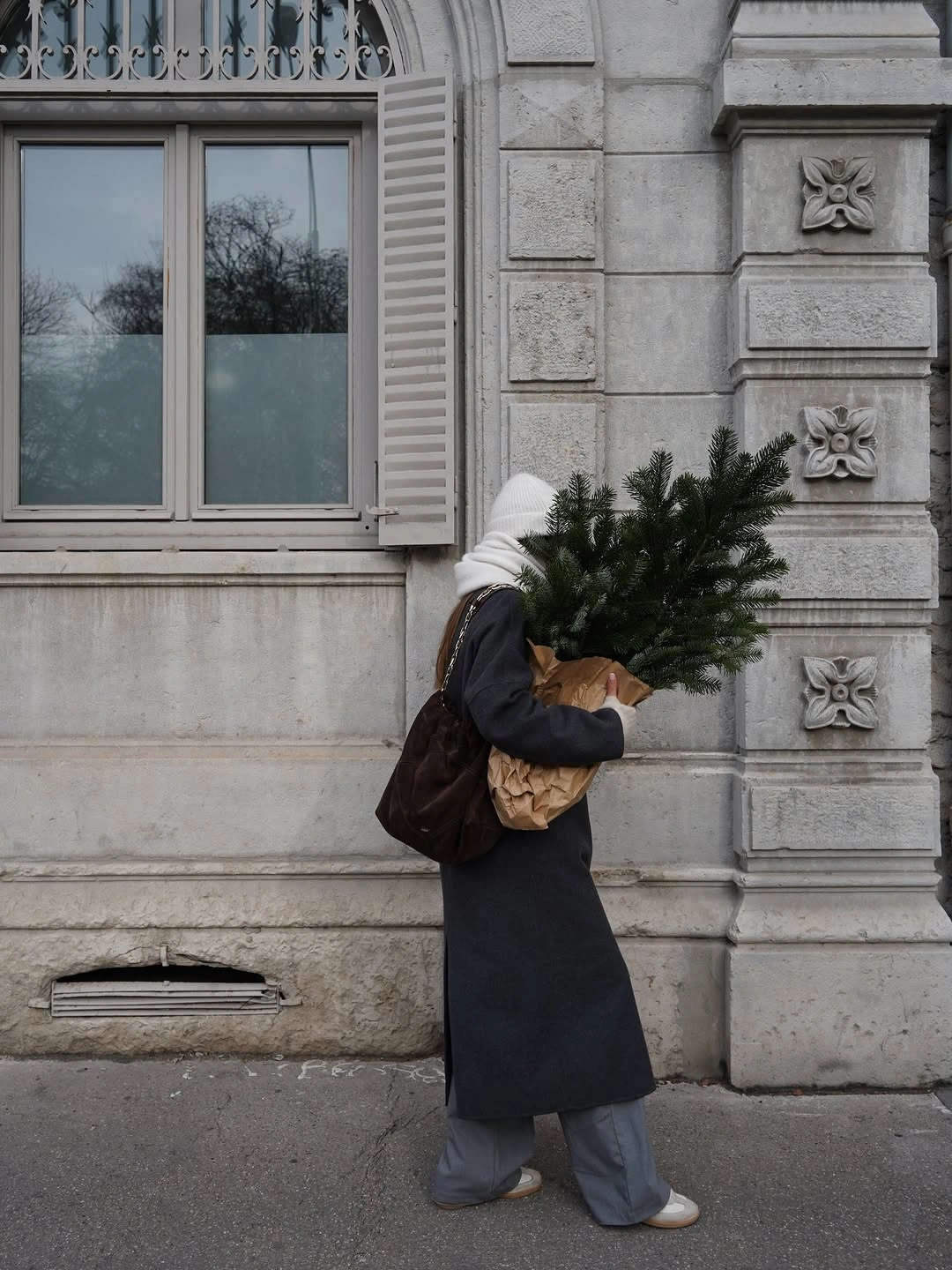 Dark long coat, gray trousers, white beanie, and pale shoes